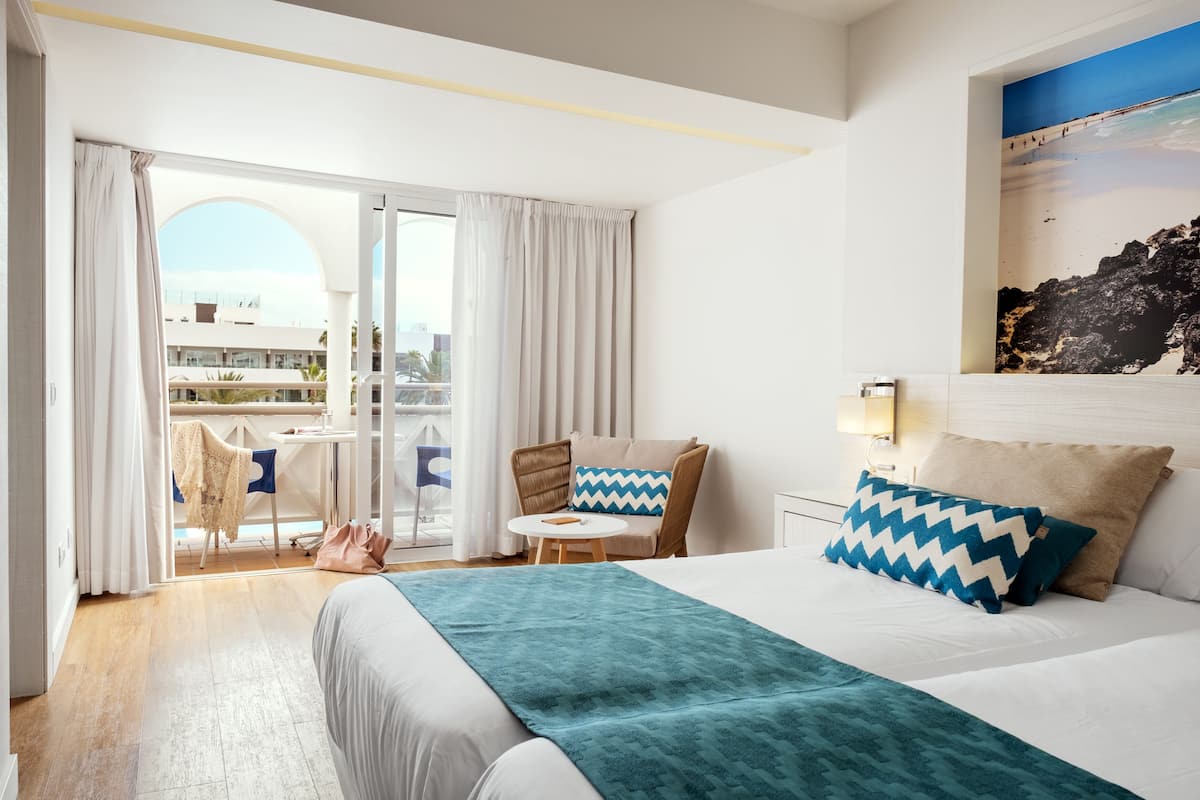 Hotellihuone, jossa on sänky, tuoli, pieni pöytä ja näkymä ulos.