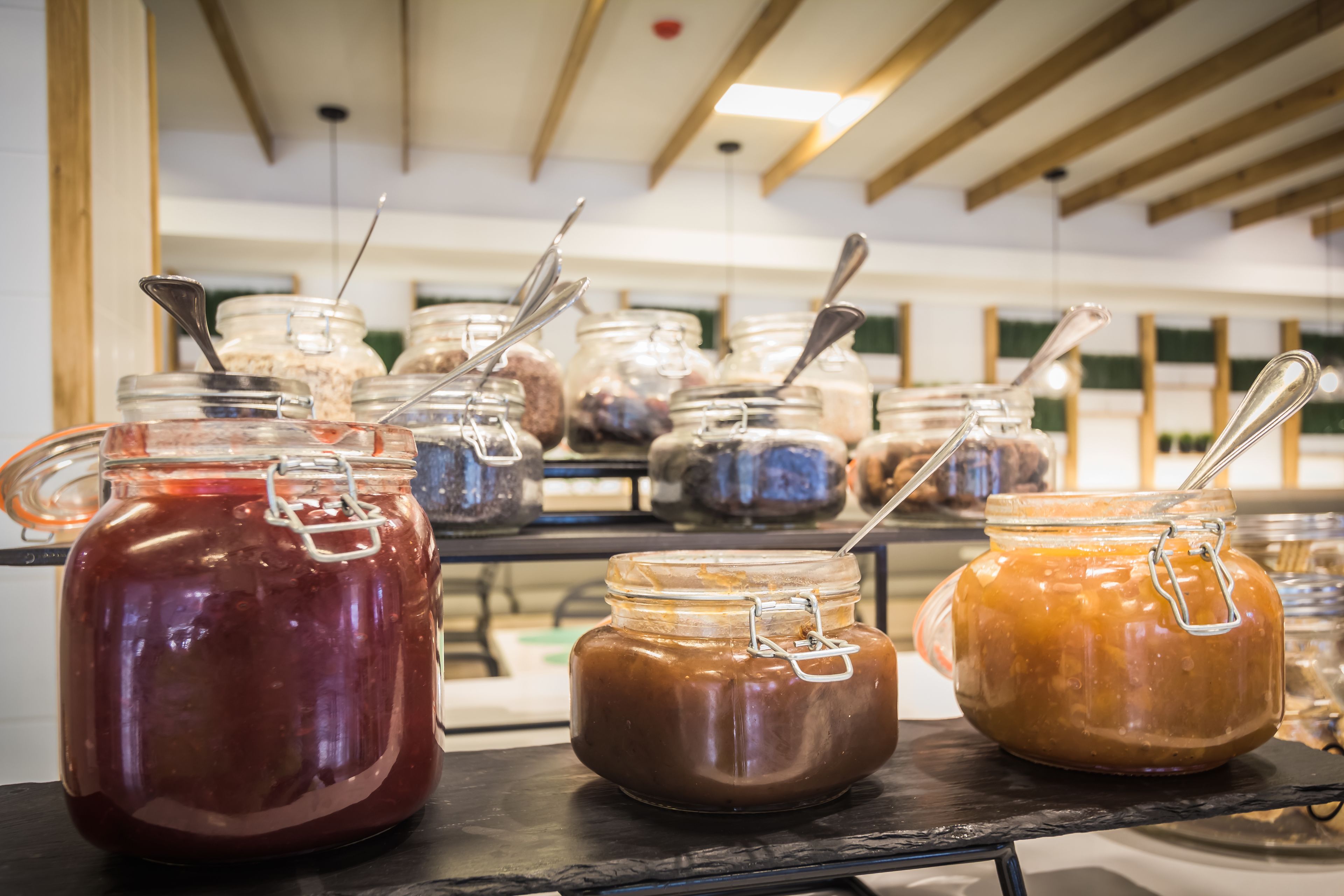 A variety of jars with metal lids and spoons on a shelf.