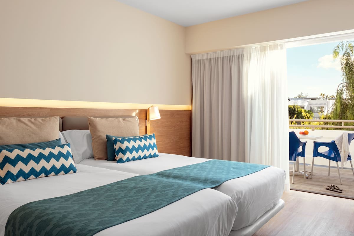 Hotellihuone, jossa on suuri sänky, parveke tuoleineen ja näkymä ulos.