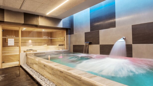 Un spa moderne doté d’un sauna en bois, d’un jacuzzi avec une cascade et d’un comptoir d’enregistrement.