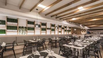 Un restaurante moderno con vigas de madera, paneles verdes en la pared y mesas y sillas ordenadas.