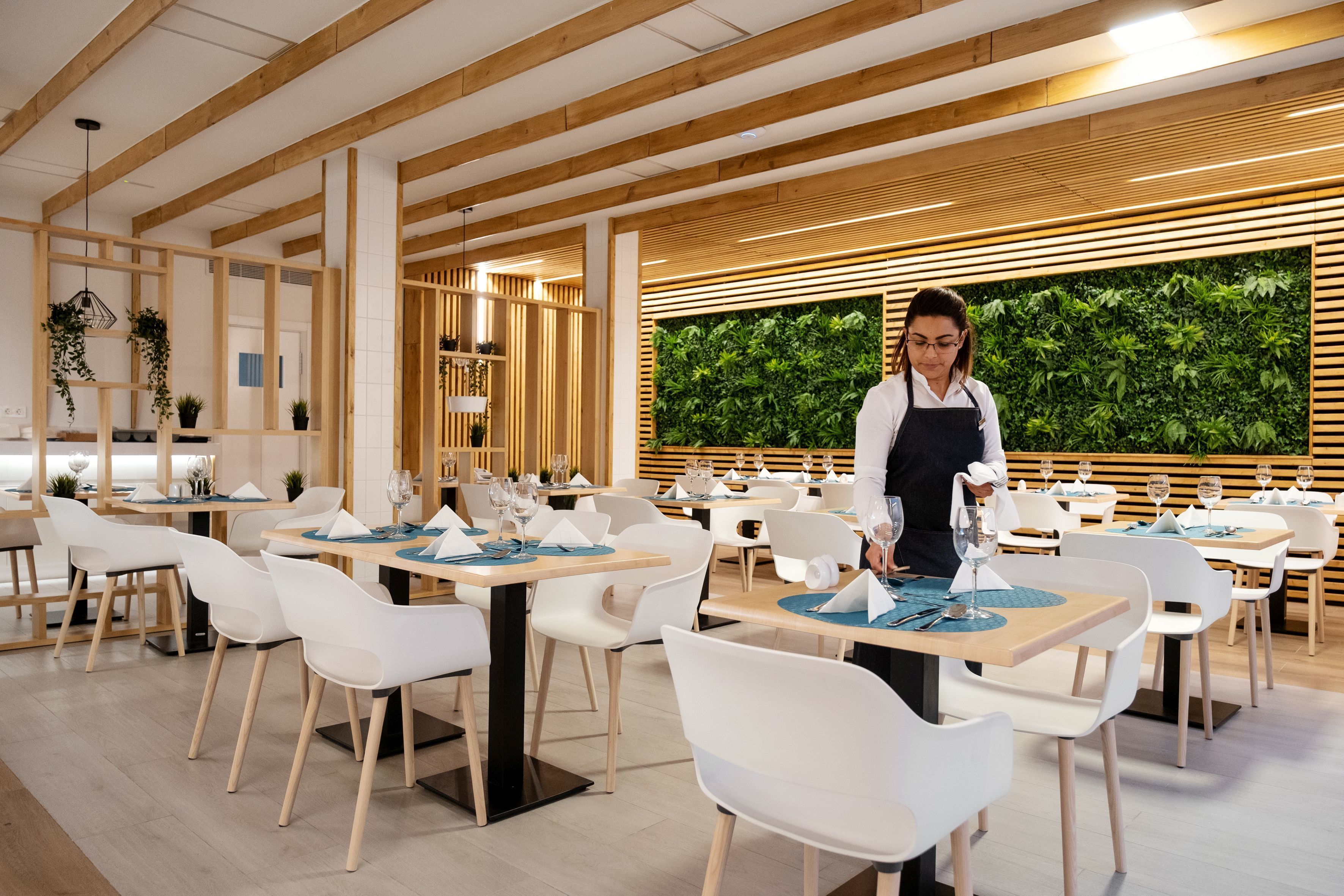 Un restaurante moderno con vigas de madera, sillas blancas y mesas dispuestas para comer.