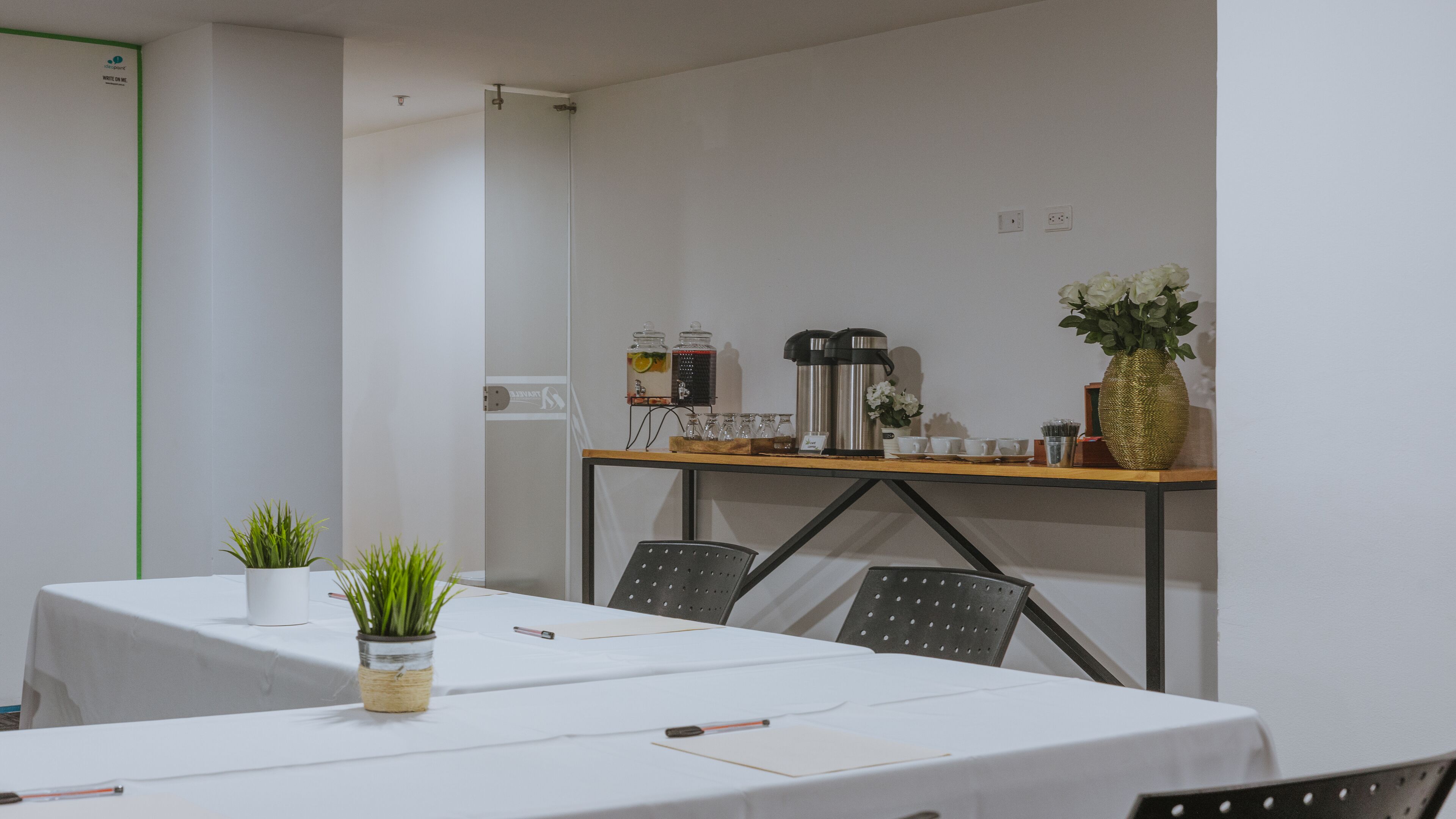 A conference room with a white table, chairs, a coffee station, and a small plant.