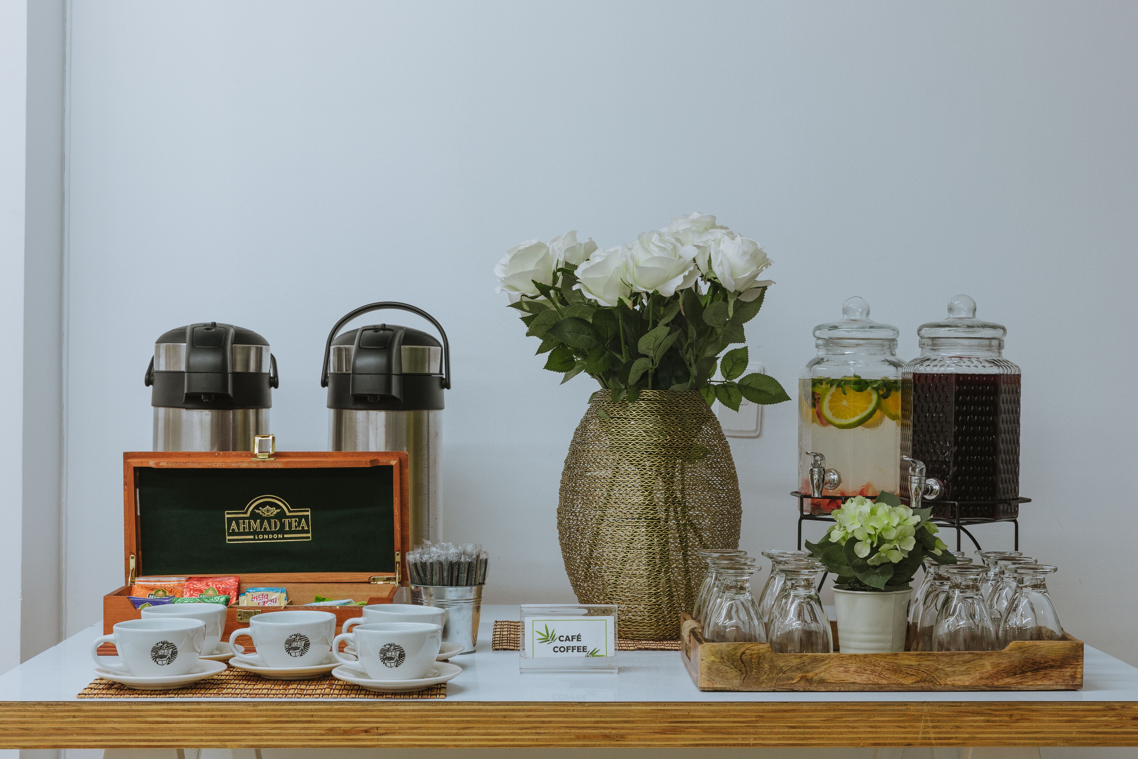 Una disposición para el desayuno con teteras, tazas, un jarrón con flores y un letrero que indica servicio de café de cafetería.