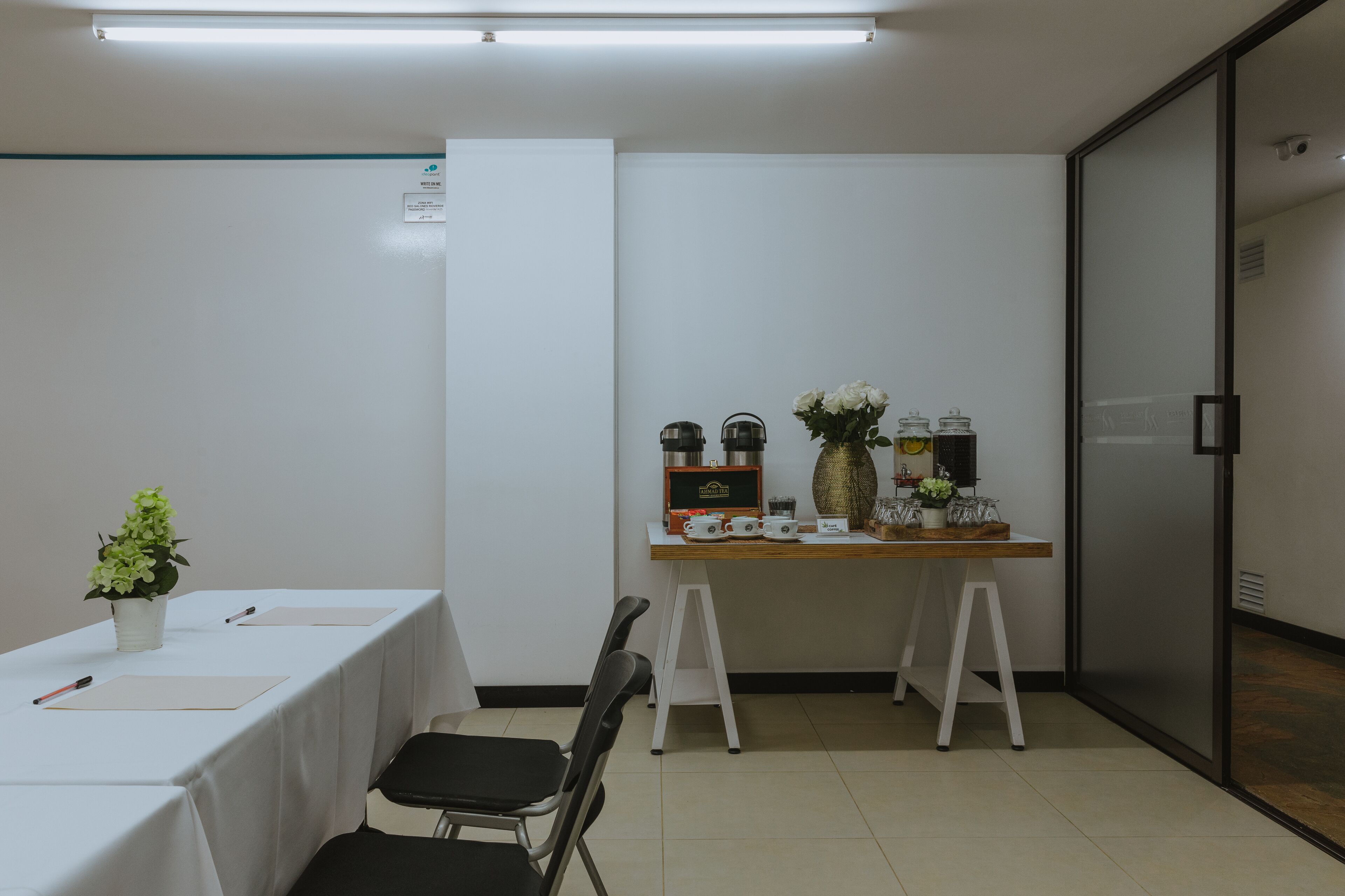 Una sala conferenze con un tavolo bianco, sedie, una piccola pianta in vaso e un tavolo espositivo con diversi oggetti.