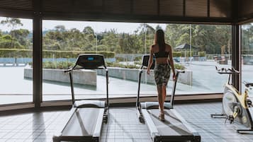 Uma academia com esteiras e uma bicicleta ergométrica, grandes janelas com vista para áreas verdes e uma piscina.
