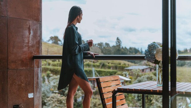 A woman standing by a balcony with a view of a rural landscape. - Travelers Rio Verde Living Suites (Rionegro)