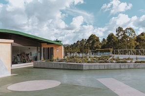 A modern building with a green roof, a covered outdoor area with exercise equipment, and a landscaped garden with trees and shrubs.