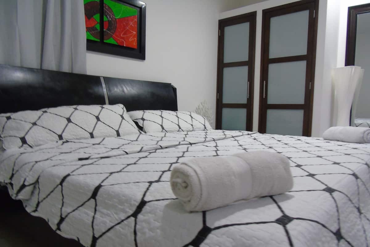 A neatly made bed with a patterned bedspread, a headboard, and a wall-mounted painting.