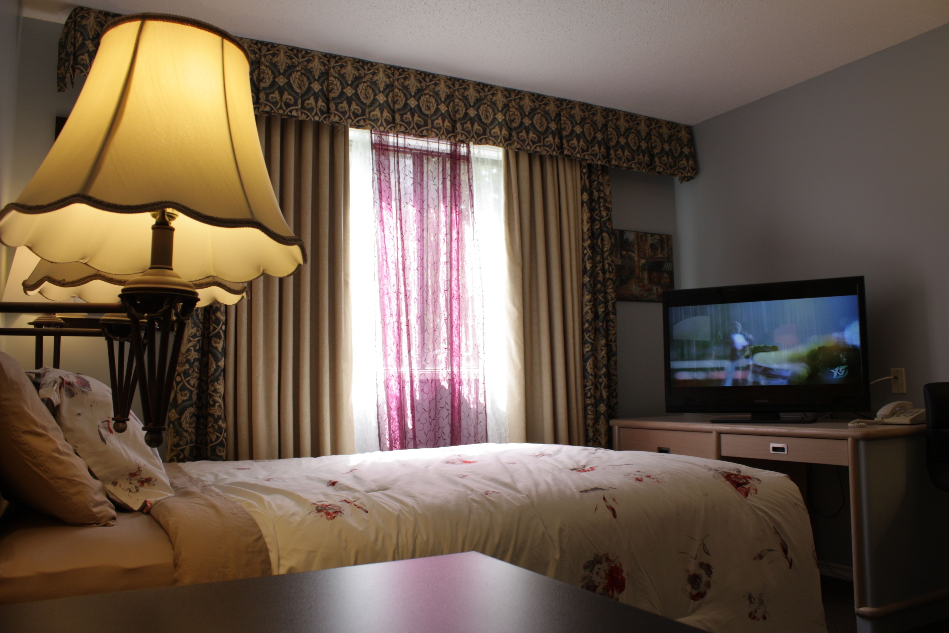 A hotel room with a bed, a desk, a television, and a lamp.