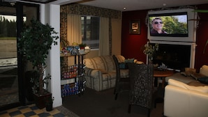 A living room with a television, a sofa, a chair, and a potted plant. - Hillcrest Motel (Swan Hills)