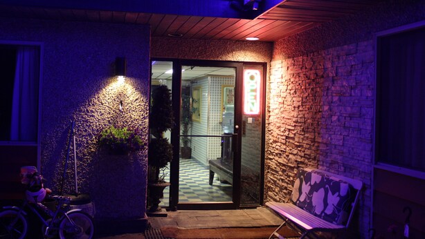 A building entrance with a stone facade, a glass door, and a neon sign. - Hillcrest Motel (Swan Hills)
