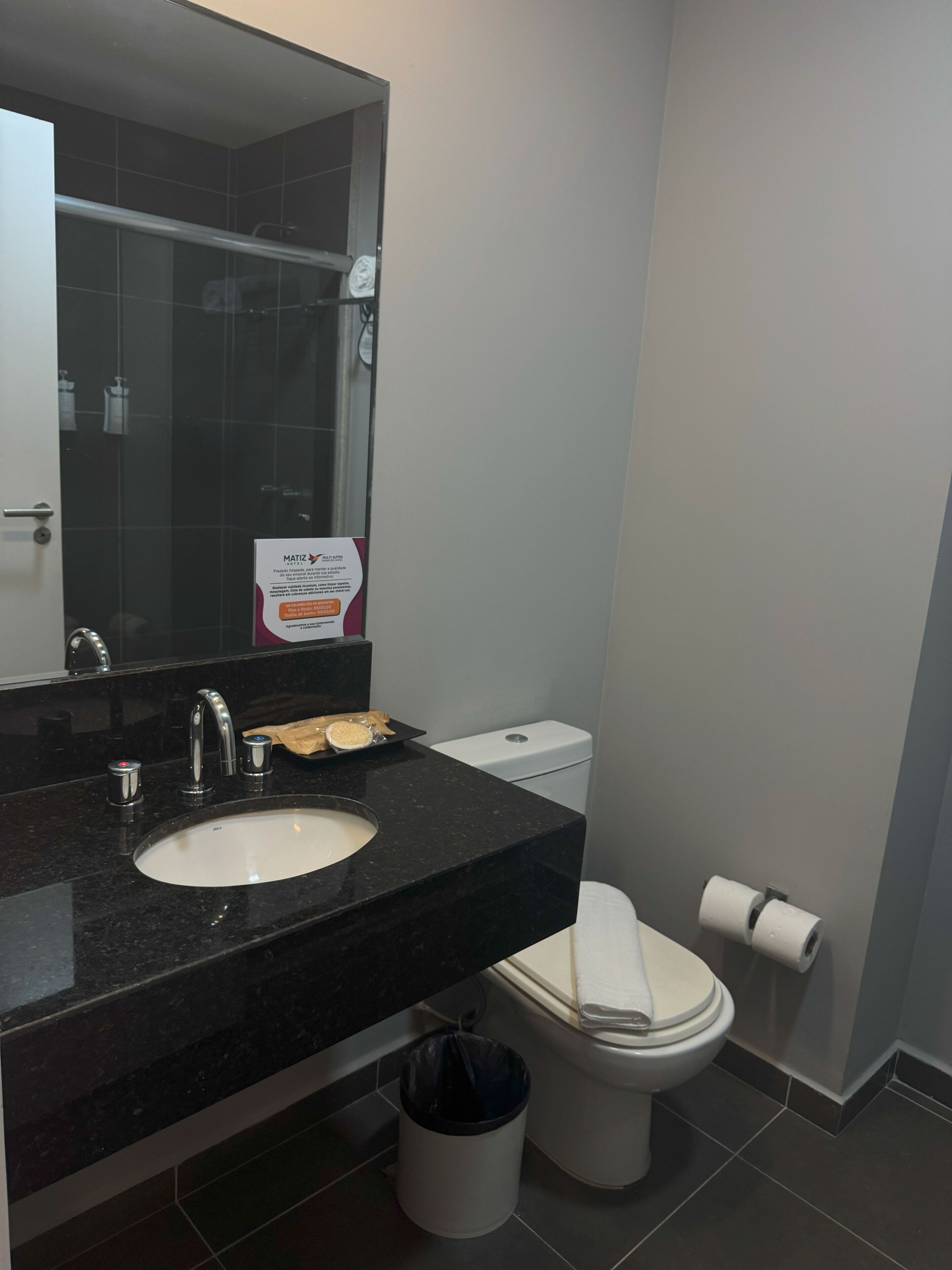 A bathroom with a black countertop sink, a mirror, a toilet, and a trash can.