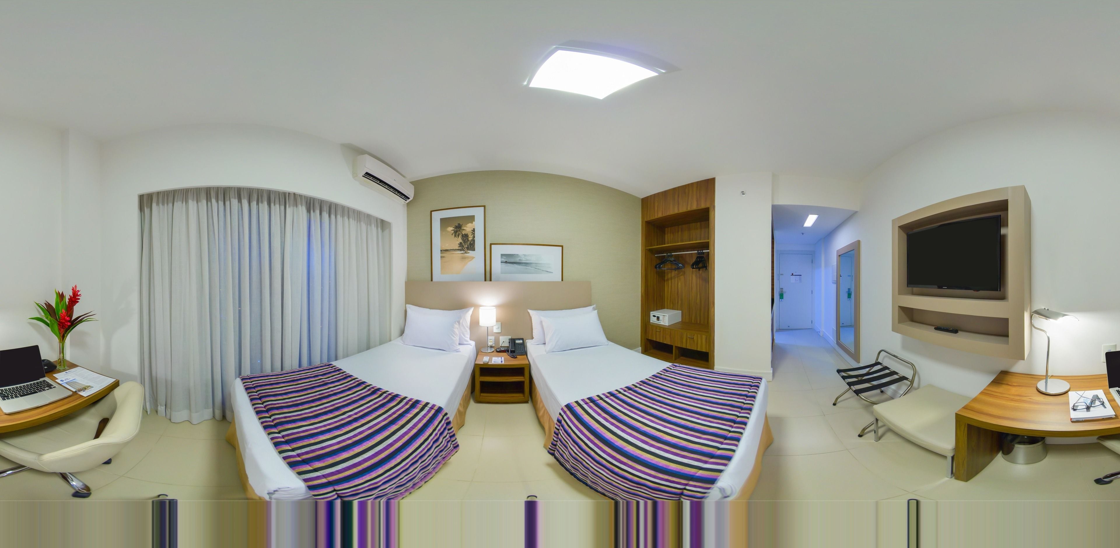 A hotel room with two beds, a desk with a laptop, a chair, a TV, and a wardrobe.