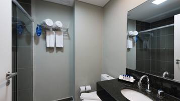 A modern bathroom with a glass shower enclosure, a white toilet, a black granite sink, and a large mirror.