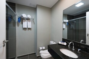 A modern bathroom with a glass shower enclosure, a white toilet, a black granite sink, and a large mirror. - Matiz Multi Suítes (Duque de Caxias)