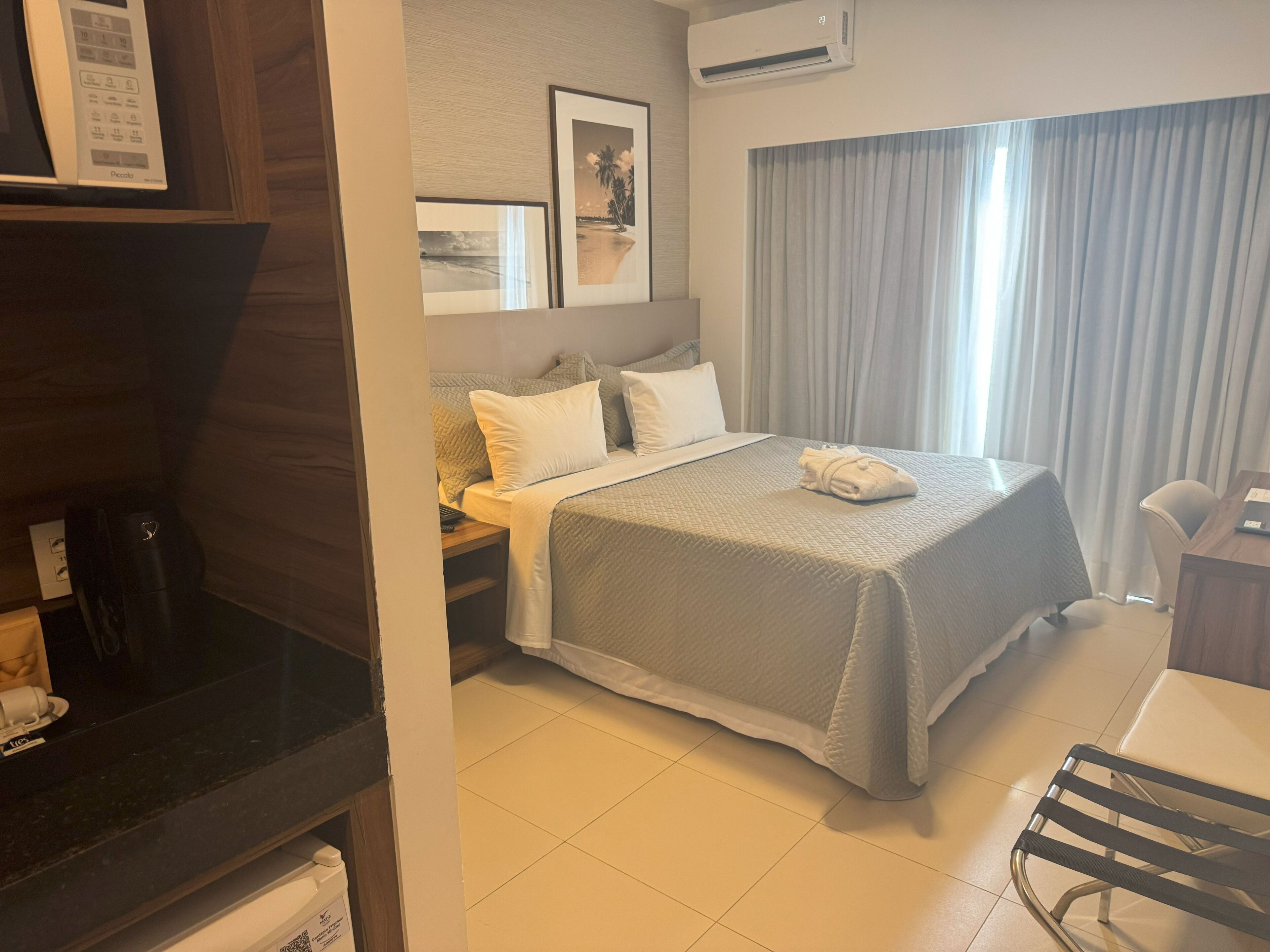 A hotel room with a bed, a desk, a chair, a TV, and an air conditioning unit.
