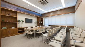A conference room with a long table and chairs, wooden shelves with books, and a large window with blinds.