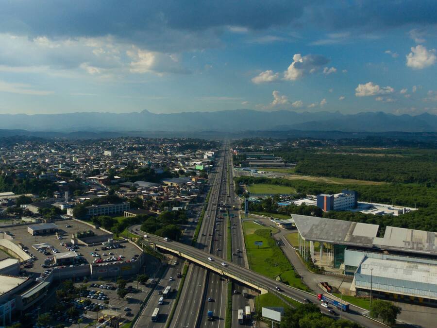 An aerial view of a city with a highway, buildings, and mountains in the background.