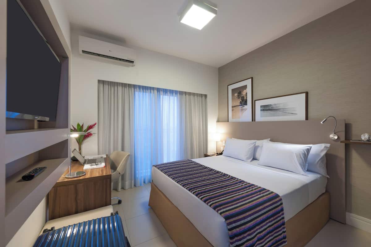 A hotel room with a bed, desk, chair, and a TV.