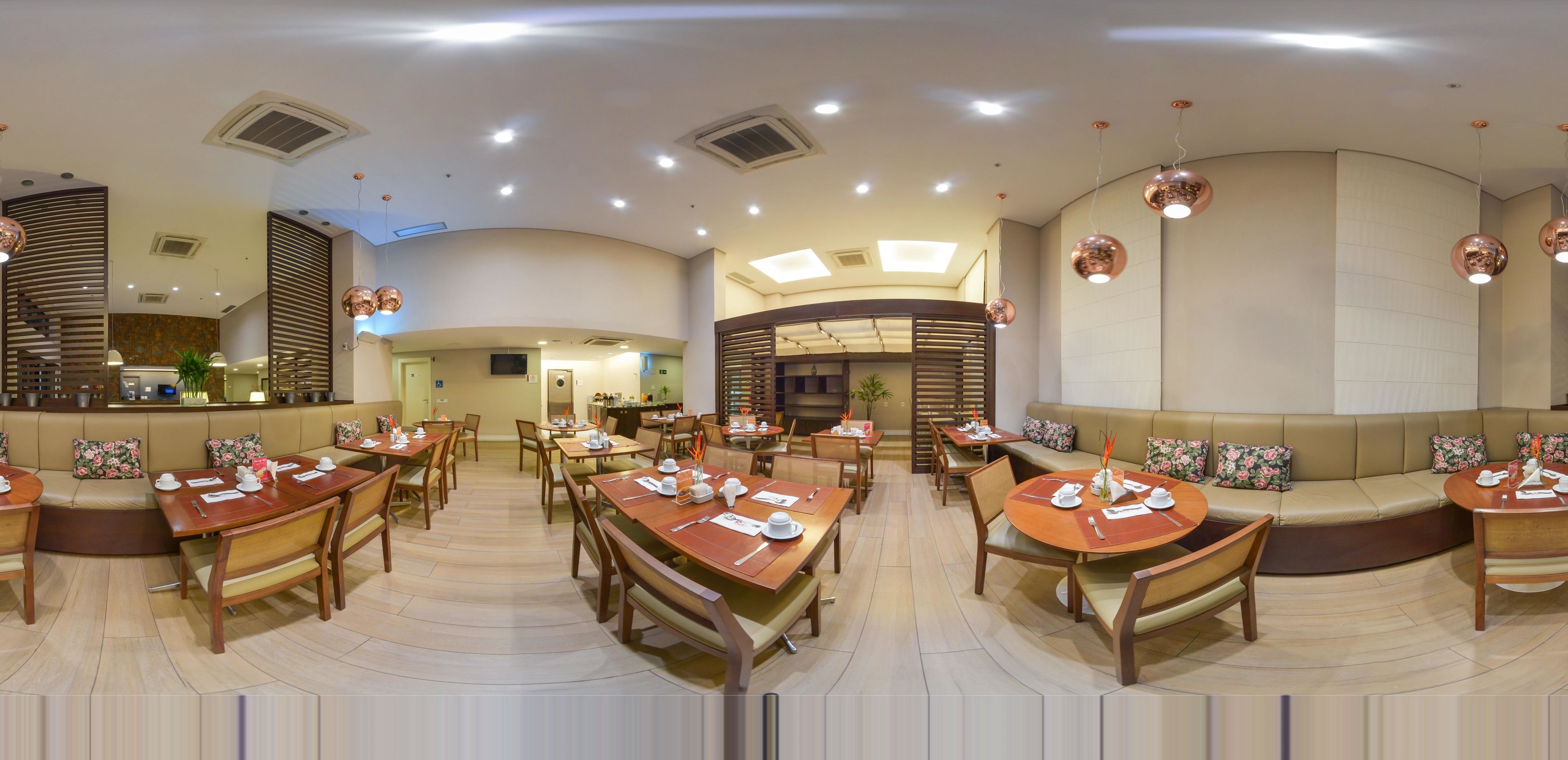 Um restaurante espaçoso com diversas áreas de refeição, incluindo mesas redondas e cabines, e uma cozinha aberta no centro.
