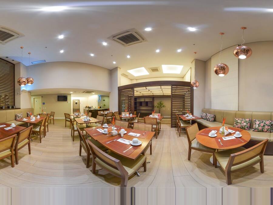 Um restaurante espaçoso com diversas áreas de refeição, incluindo mesas redondas e cabines, e uma cozinha aberta no centro.