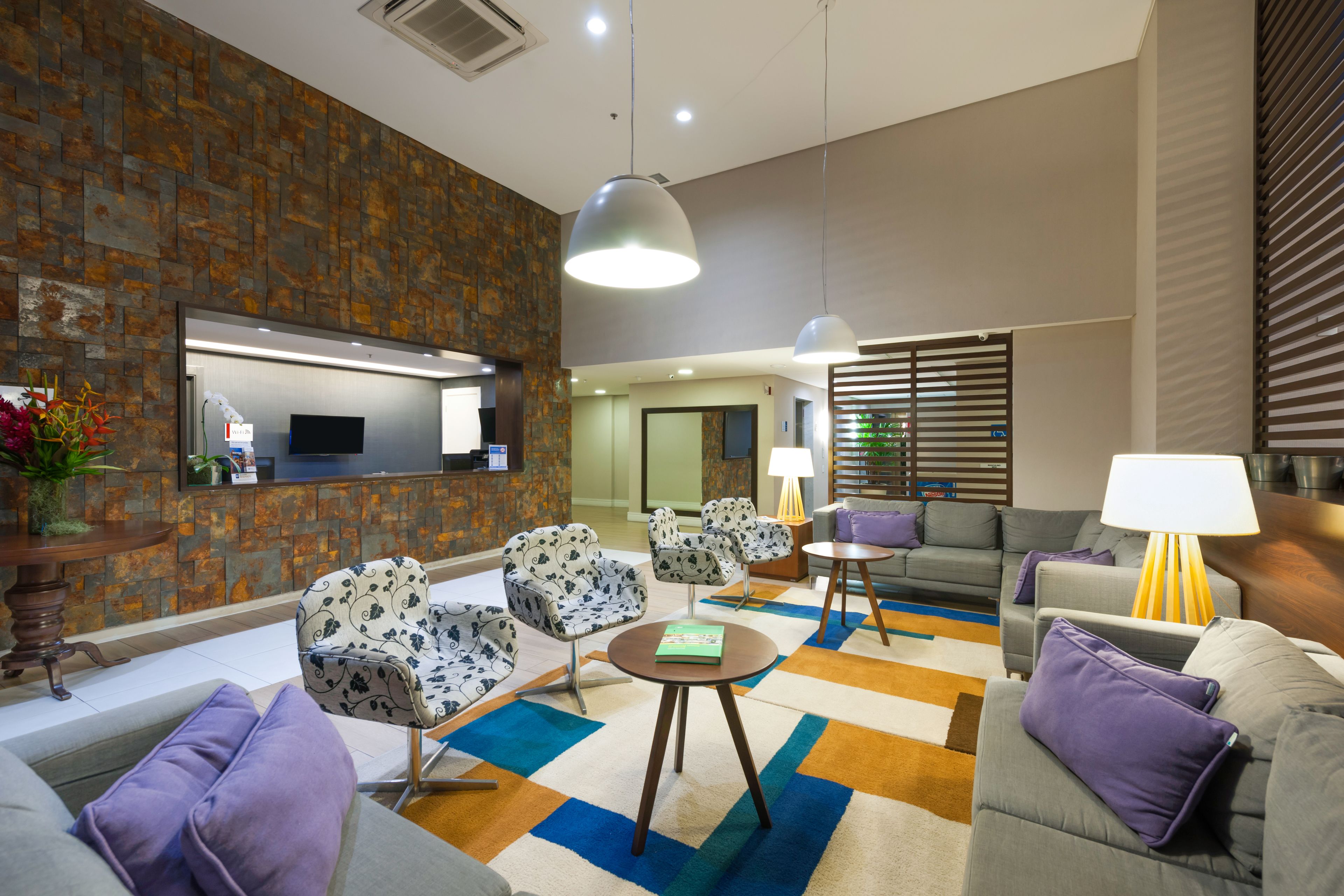 Un vestíbulo moderno con una pared de piedra, un mostrador de recepción y zonas de estar con sillones y un sofá estampados.