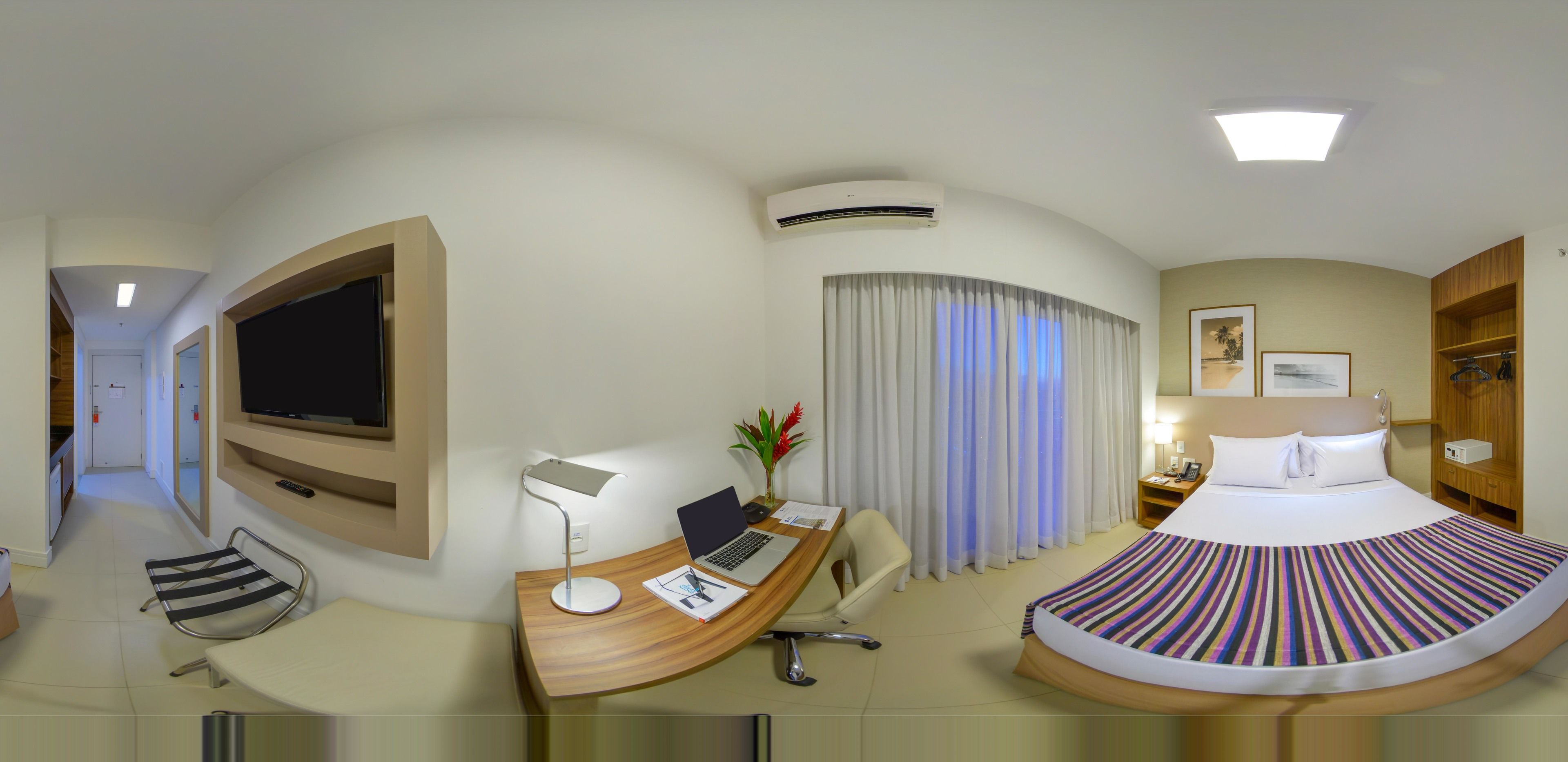 A hotel room with a bed, desk, chair, TV, and curtains.