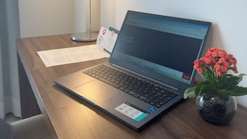 A laptop on a wooden desk with a flower vase, a lamp, and a printed document.