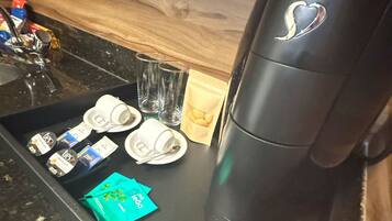 A coffee machine with a heart logo, a tray with coffee pods, a tea bag, and a glass.