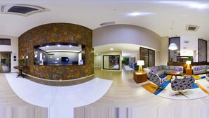 Un moderno vestíbulo de hotel con un mostrador de recepción curvo, zonas de estar y una escalera visible.