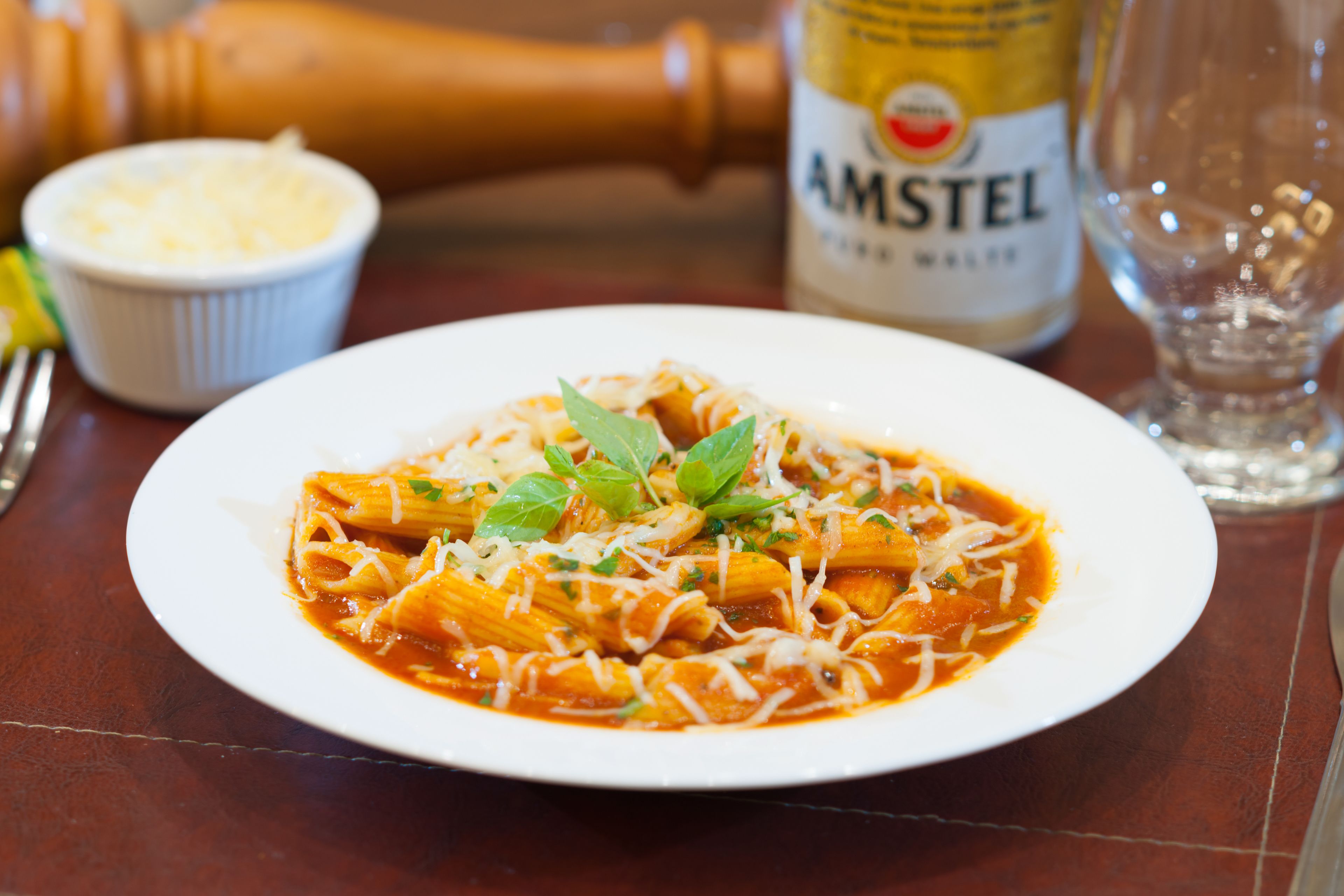 A plate of pasta with a bottle of Amstel beer and a salt shaker in the background.