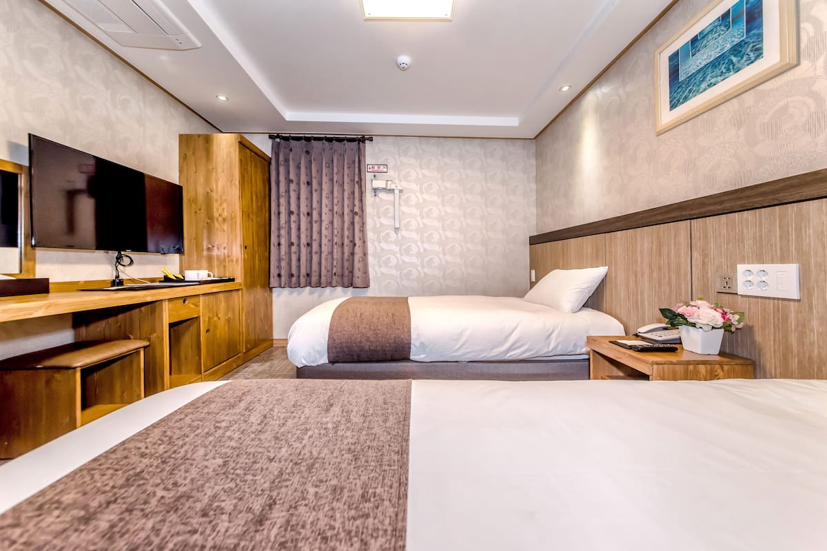 Une chambre d’hôtel avec un lit, un bureau avec une télévision, une petite table de chevet avec un téléphone et des fleurs, et un radiateur fixé au mur.