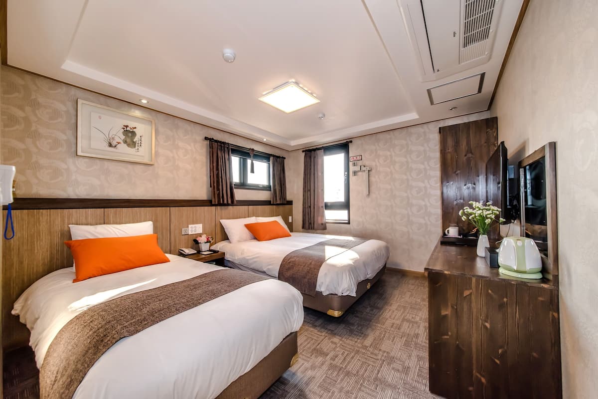 Une chambre d’hôtel avec deux lits, une commode en bois, un téléviseur à écran plat et un luminaire au plafond.