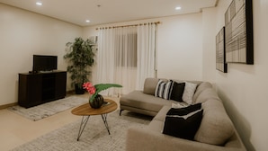 A living room with a sofa, a coffee table, a TV on a stand, a potted plant, and a curtain.