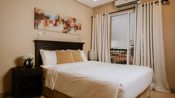 A neatly made bed with white linens and two pillows, a bedside table with a vase of flowers, and a large abstract painting on the wall.