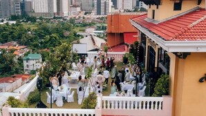 A rooftop event with tables and chairs, surrounded by greenery and buildings in the background.