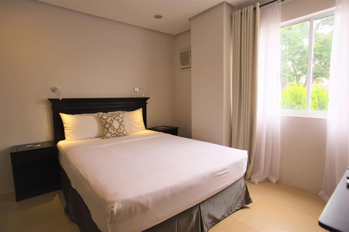 Una cama bien hecha con cabecera, mesita de noche y ventana con cortinas.