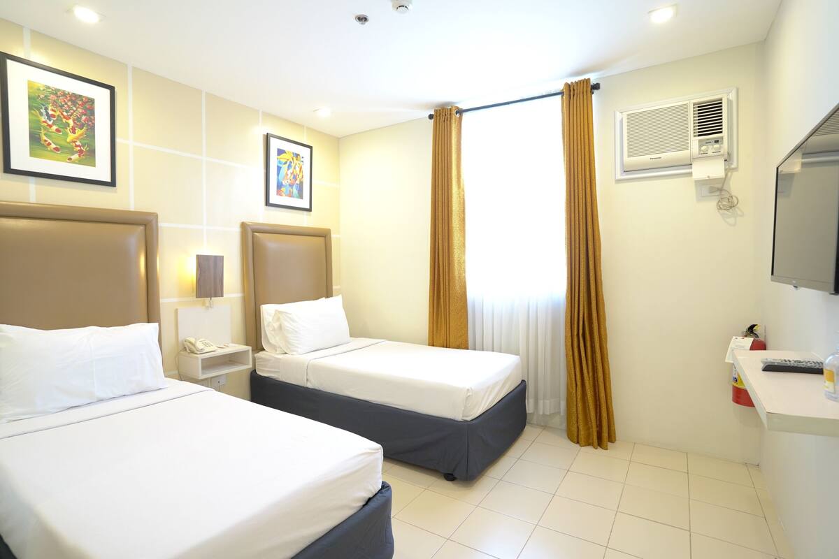 Habitación de hotel con dos camas, un escritorio, teléfono, unidad de aire acondicionado y televisión.