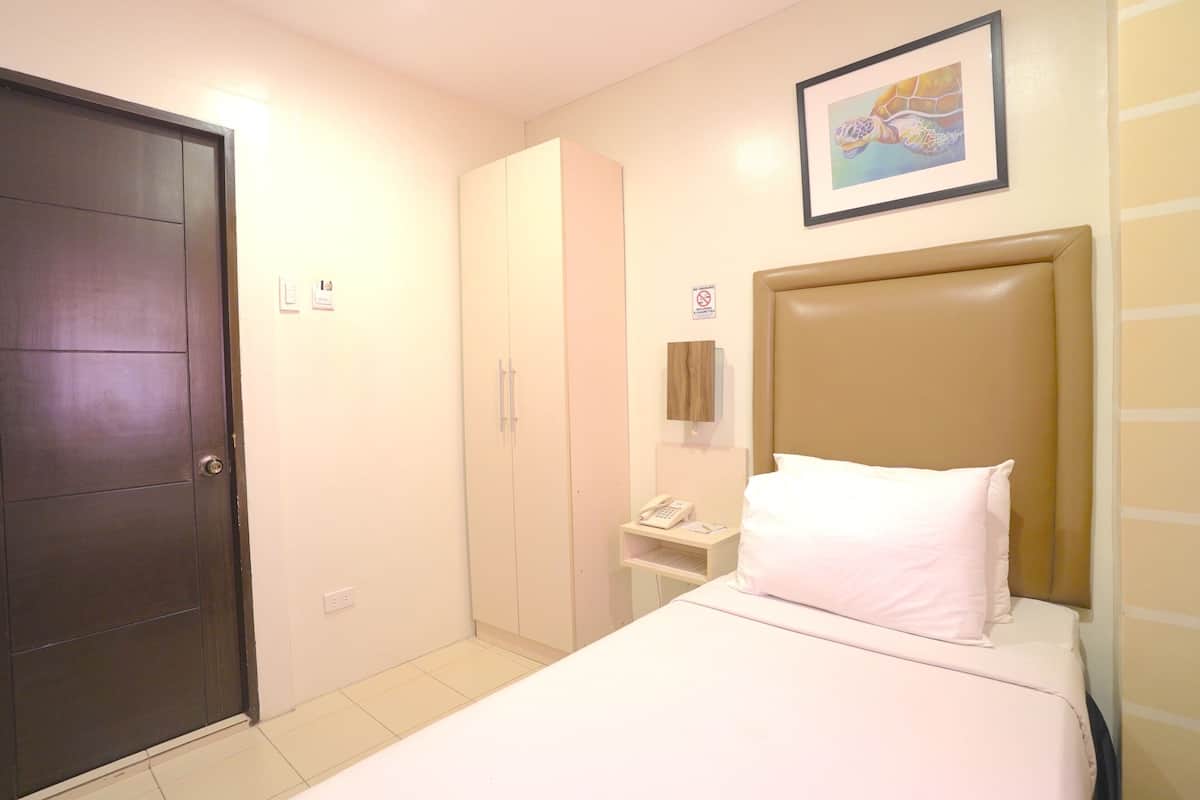 Un dormitorio con cama, armario, escritorio con teléfono y un cuadro en la pared.
