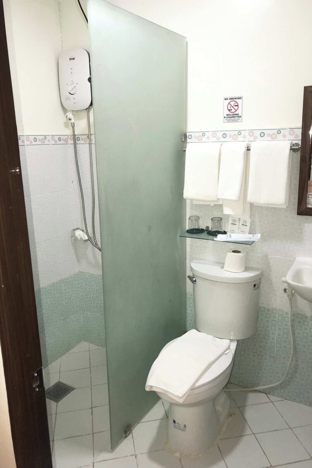 Un baño pequeño con inodoro, ducha y lavamanos. Hay un cartel de prohibido fumar en la pared.