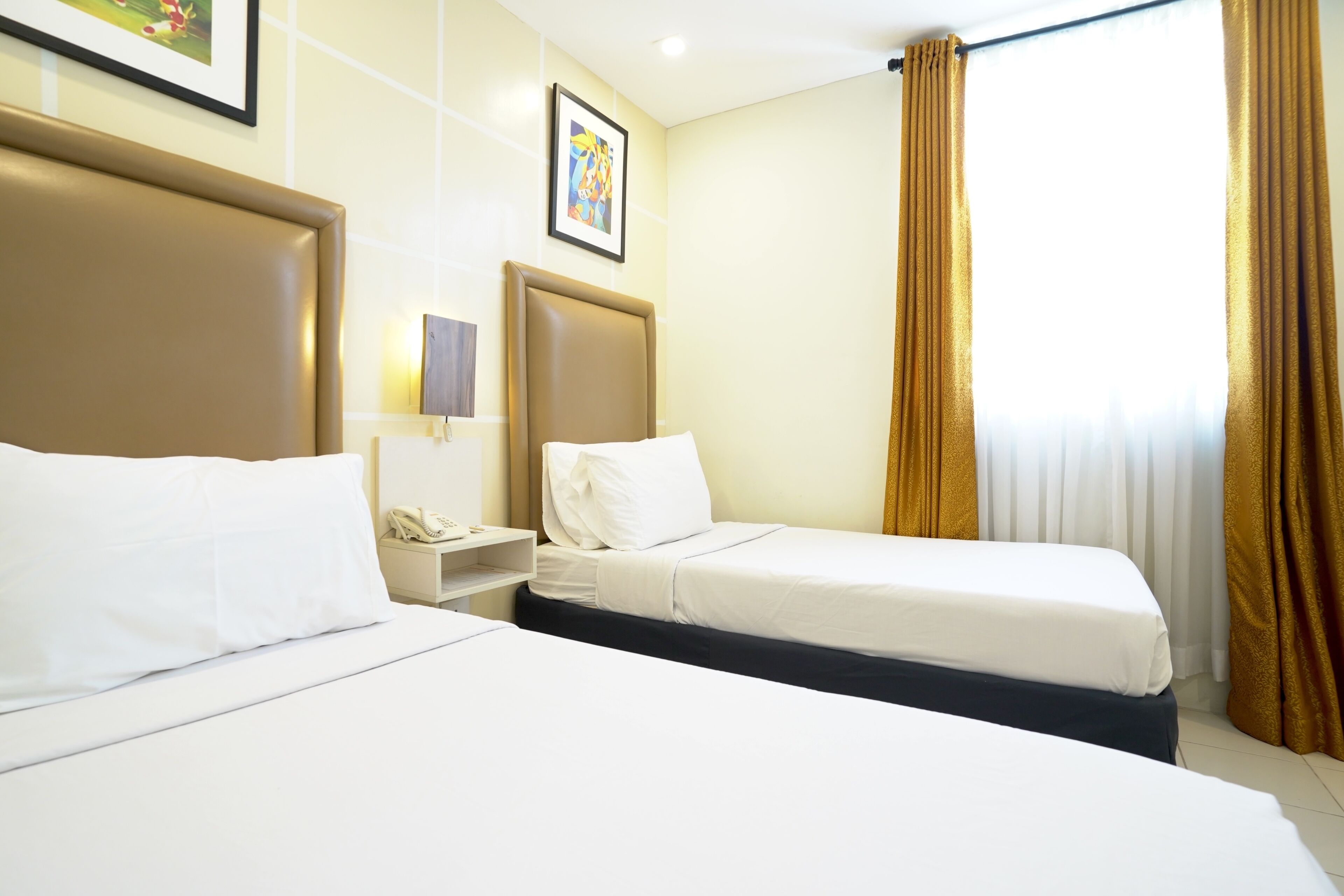 Habitación de hotel con dos camas, una mesita de noche con teléfono, un cuadro en la pared y una ventana con cortinas.