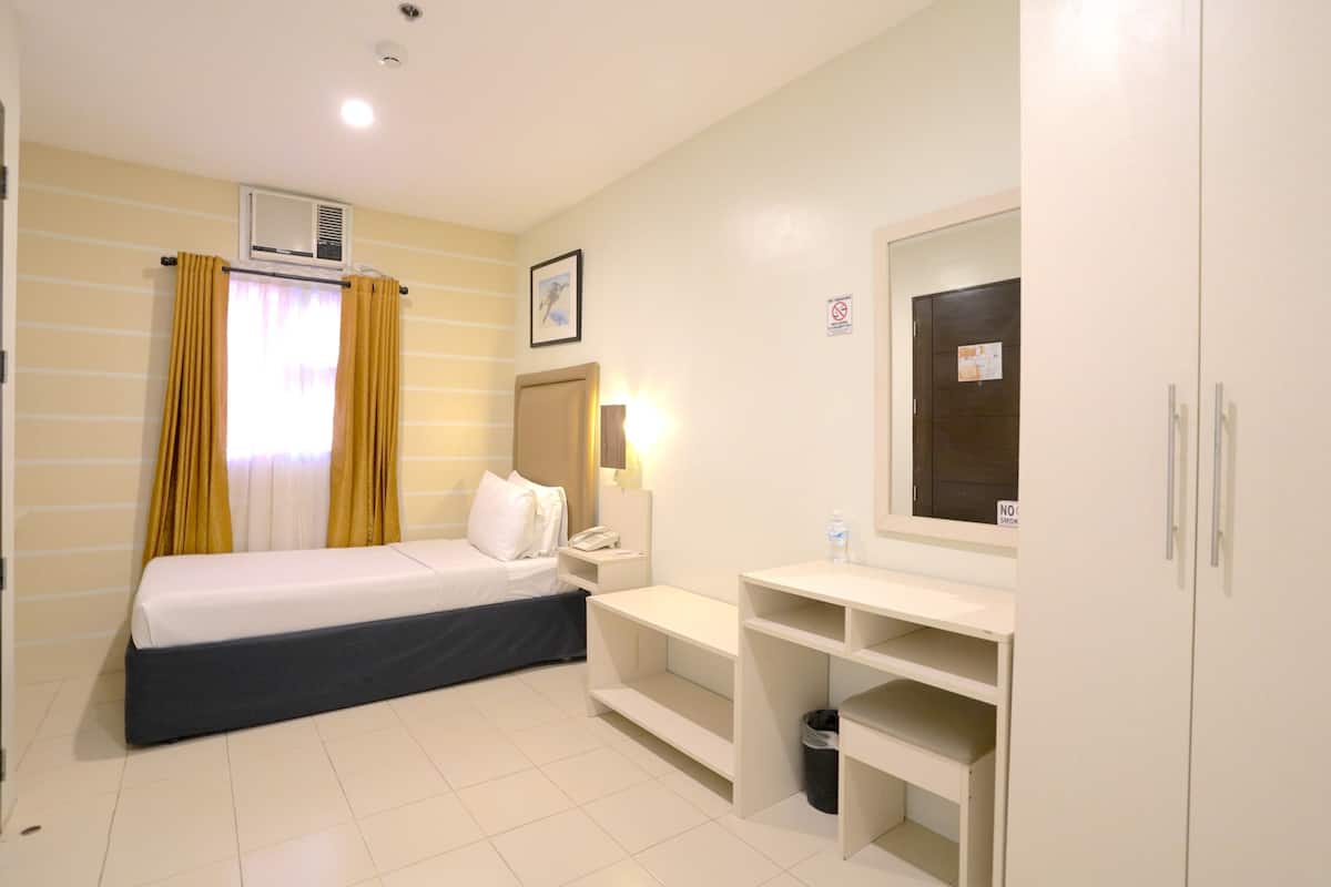 Habitación de hotel con cama, escritorio, espejo, armario y cubo de basura.