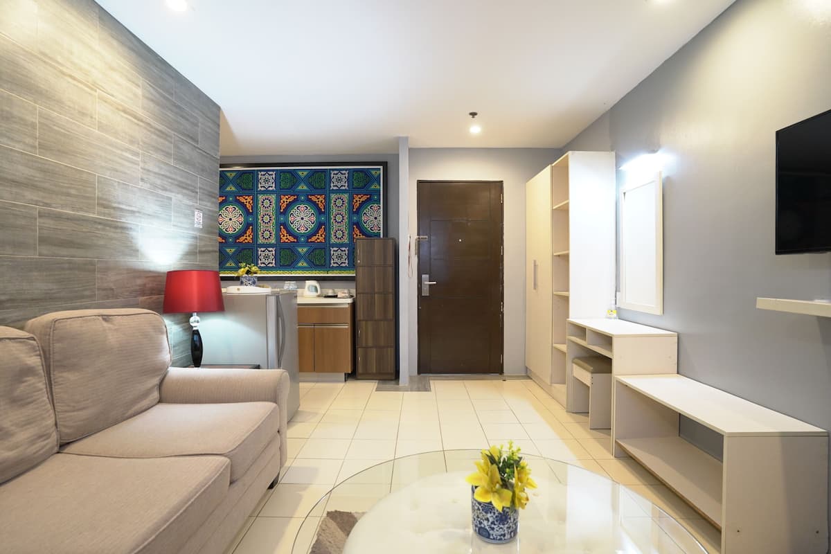 Una sala moderna con sofá, una mesa de centro con flores, una zona de cocina y un televisor montado en la pared.