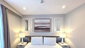 A hotel room with a bed, two bedside tables, a wall-mounted artwork, and a ceiling light. - Tom's Cabin Hotel (Cebu City)