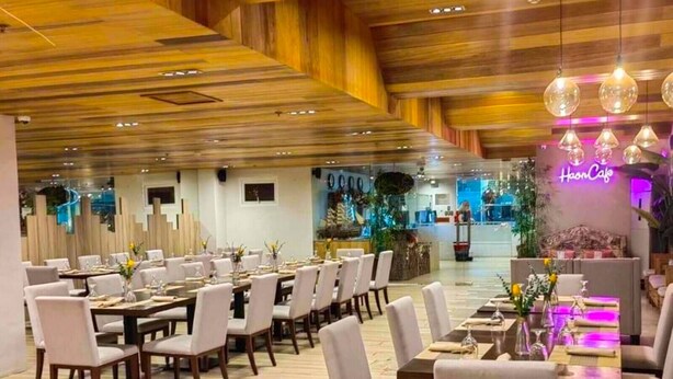 A restaurant with wooden ceiling panels, white chairs, and tables set for dining. - Tom's Cabin Hotel (Cebu City)