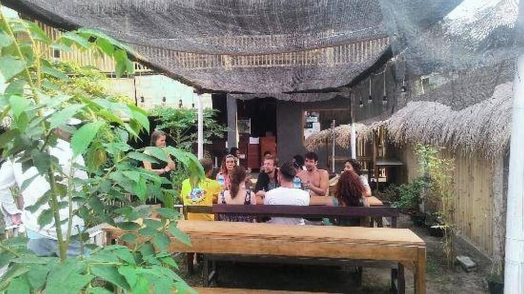 A group of people seated at an outdoor wooden table under a thatched roof structure.