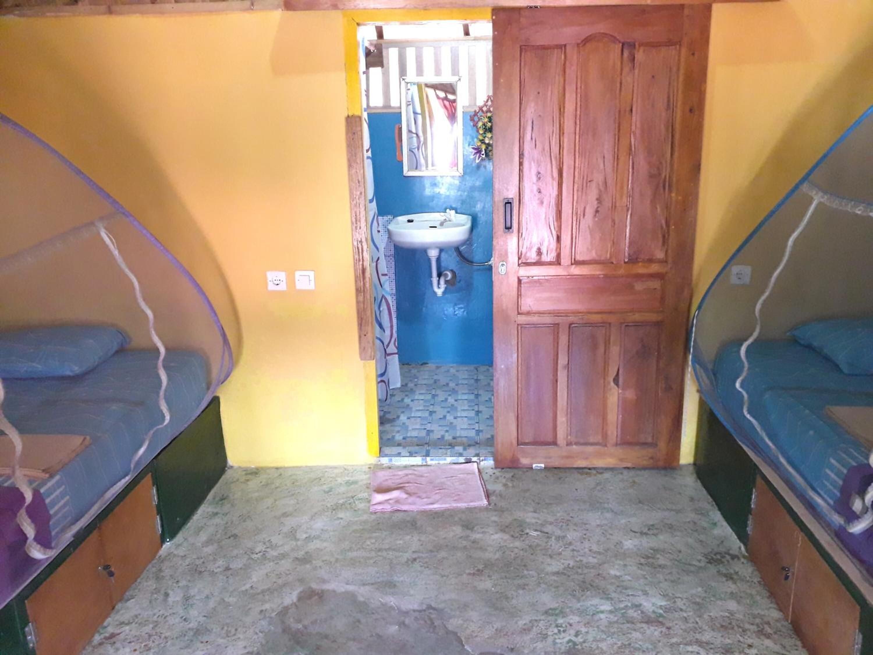 A small, compact room with two bunk beds, a wooden door, a sink, and a small window.