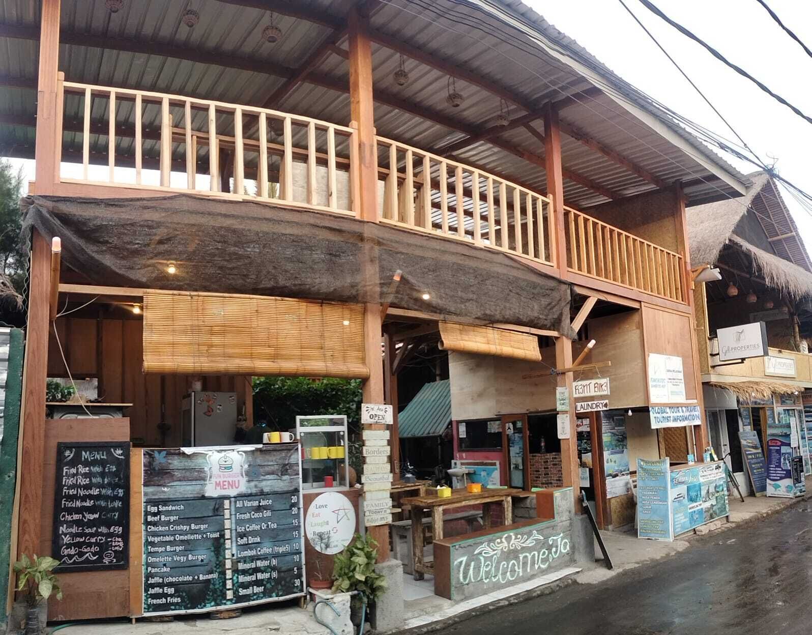 Un restaurante con fachada de madera, zona de estar al aire libre cubierta y un letrero que da la bienvenida a los visitantes.