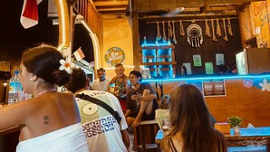 Um bar com decoração em madeira, um letreiro de neon e um balcão com garrafas.
